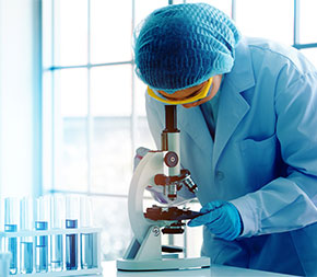 woman in gloves and sterile lab coat looks in microscope