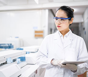 woman in labcoat and goggles carries tablet