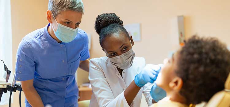 woman working on patient's teeth with dentist overseeing work
