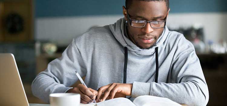 man in sweatshirt taking notes in front of laptop