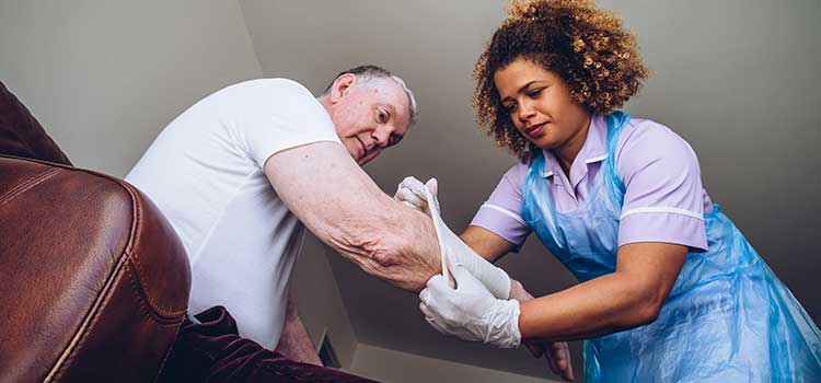 medical assistant treating wound on elderly male patient's arm