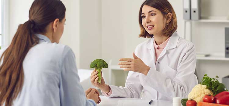 woman holding head of broccoli and taking with a patient in an office