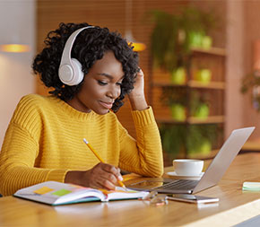 person at desk with laptop recording in notebook