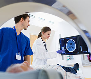two medical staff look at brain scan of patient laying down