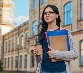 female student holding folders and coffee and walking by hospital