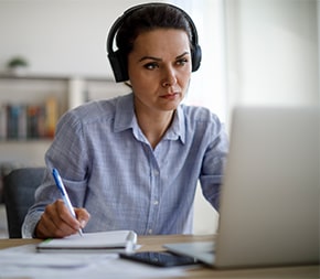 professional with headphones takes notes from laptop