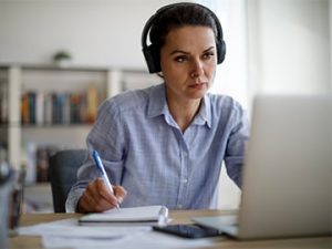 professional with headphones takes notes from laptop