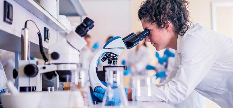 woman in lab looking through microscope