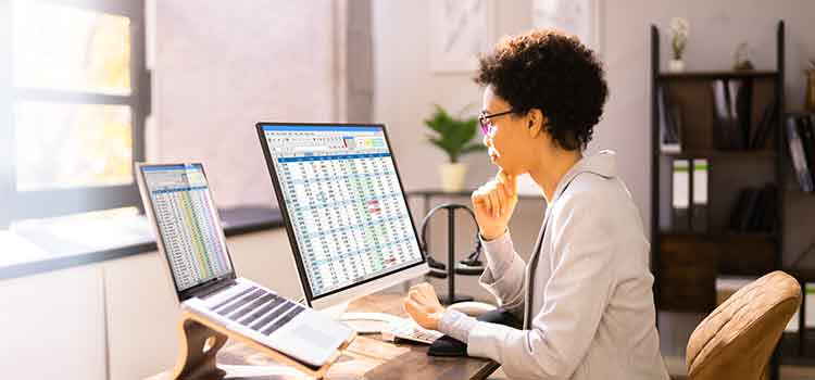 woman at desk looking at two screens with medical billing data