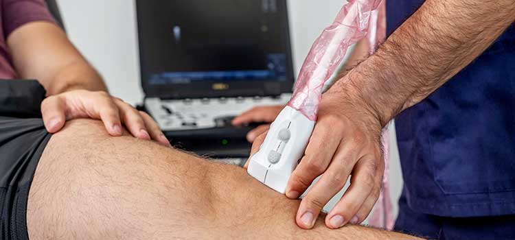 close-up of man performing ultrasound on patient's knee