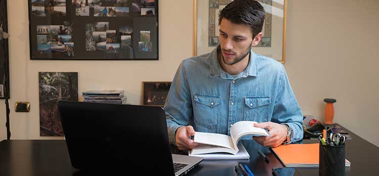 man looking at textbook and laptop