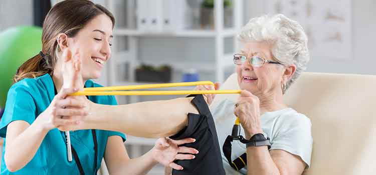 physical therapy assistant helping older woman with resistance band