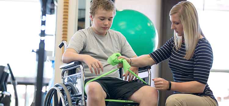 physical therapy assistant helping chhild in wheelchair with strengthening exercises