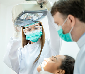 masked dental assistant adjusts light for dentist performing procedure