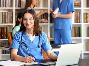 a medical assistant student works on her laptop in a library and smiles at the camera