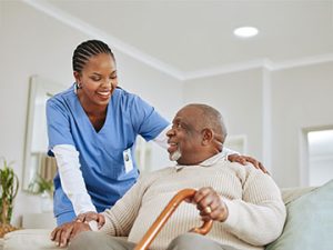 a medical assistant smiles and talks with an elderly gentleman patient with a cane