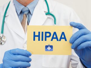 doctor in lab coat and blue sanitary gloves holding yellow card with HIPPA written on it