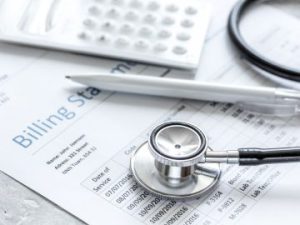 a medical billing statement rests on a table underneath a stethoscope