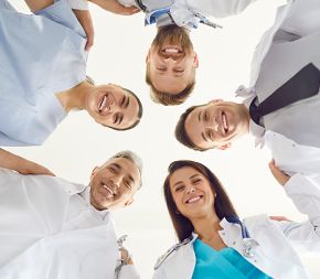medical professionals in white and blue scrubs standing in a circle looking down and smiling