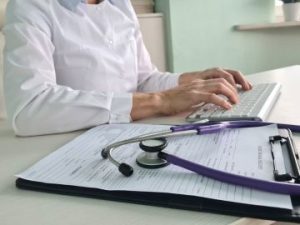 a healthcare professional uses a clipboard of doctors' notes to code procedures on a keyboard